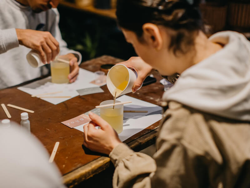 A woman in a hooded top pours wax into a container at a candle making class